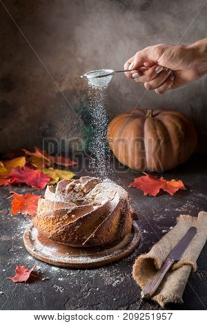 Bundt cake with saffron and rum covered with white glaze on rustic background with autumn decorations