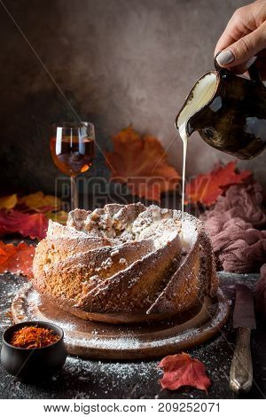 Bundt cake with saffron and rum covered with white glaze on rustic background with autumn decorations