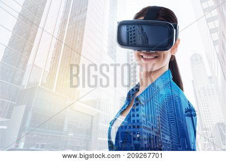 Mood-boosting game. Cheerful young woman standing half-turned, using a VR headset and smiling at the camera