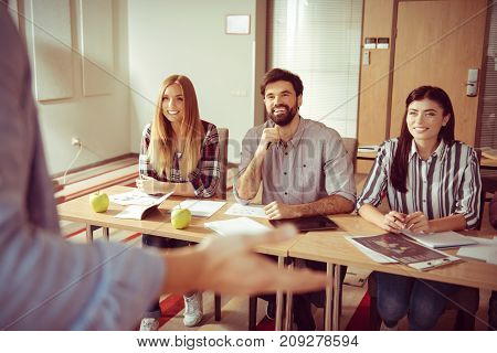 Informal atmosphere. Happy positive young people sitting at the desks and smiling while listening to their colleague