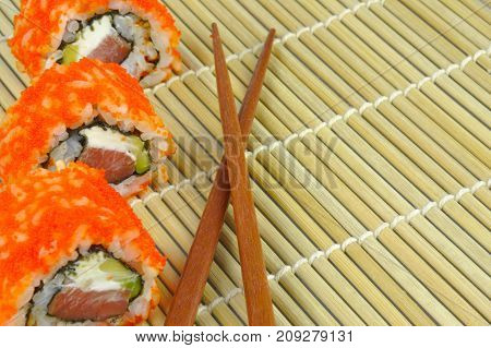 Sushi roll - avocado, cream cheese, omelette, masago roe - on bamboo mat with chopsticks