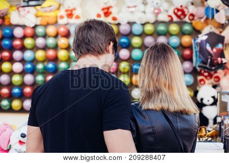 Attractive young hipster couple choose which game to play at county fair carnival popping colorful baloons to win prize on romantic date during summer break