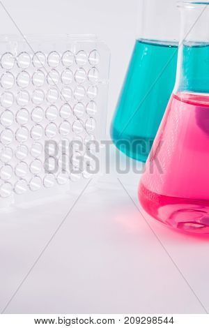 research, science and clinic background. 96 well micro plate and  laboratory beakers with colorful liquids and reagents.