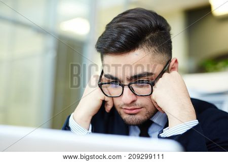 Young man in eyeglasses concentrating on reading online data for new project