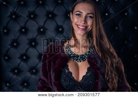 Luxurious young beautiful girl with beautiful adornments smiling at the camera on a dark background