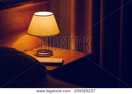 Electric lamp and book on bedside table in bedroom selective focus