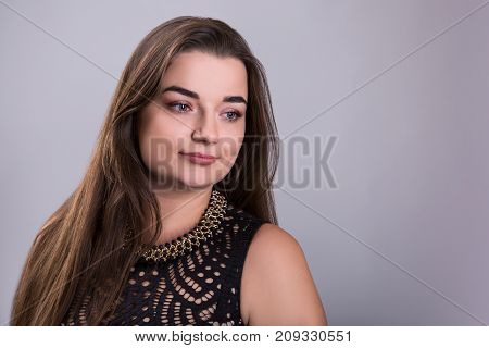 Portrait of a plus size female model posing in black dress over grey background. Beautiful woman with curvy figure.