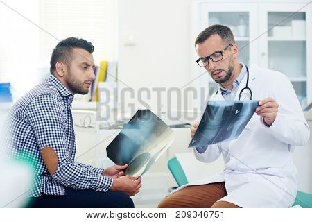 Serious radiologist showing x-ray images of joints to patient and giving him consultation