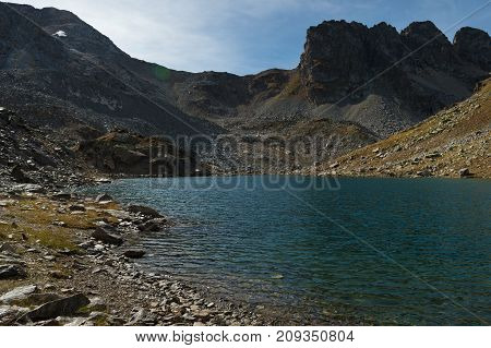 landscape of a high mountain lake with daylight with translucent stones through the water at the bottom of the lake and sharp rocks in the background. High-altitude lake in arkhyz. North Caucasus