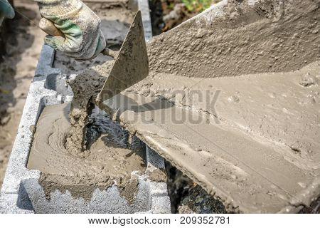 Closeup of mason hand pouring out mortar into concrete shuttering blocks from wheel-barrow