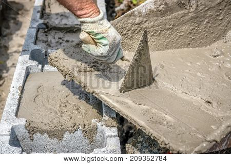 Closeup of mason hand pouring out mortar into concrete shuttering blocks from wheel-barrow
