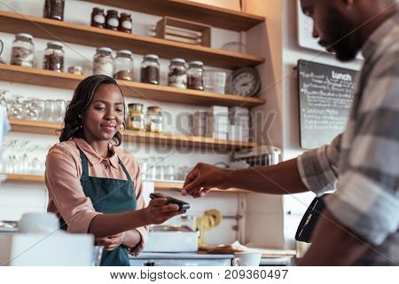 Customer using a bank card and nfs technology to pay a barista for a purchase at a cafe