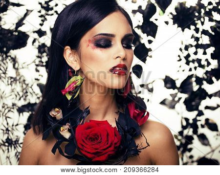 pretty brunette woman with rose jewelry, black and red, bright make up kike a vampire closeup red lips, halloween concept