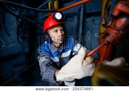 young coal miner is underground in a mine for coal mining in overalls against the backdrop of mining equipment. concept of repair of industrial equipment.