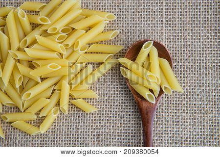 Penne raw pasta in wooden spoon on sack rustic background . Natural and healthy food concept