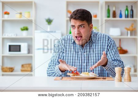 Young husband eating tasteless food at home for lunch