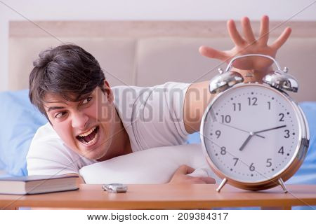 Man in bed frustrated suffering from insomnia with an alarm cloc