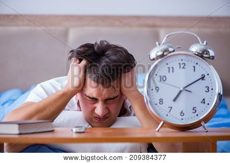Man in bed frustrated suffering from insomnia with an alarm cloc
