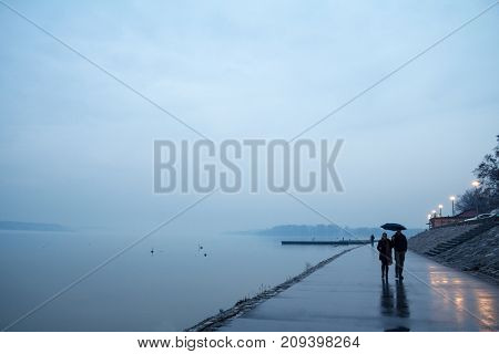 BELGRADE SERBIA - JANUARY 18 2015: People walking with umbrellas near the Danube river during a heavily foggy and rainy winter afternoon in Zemun a northern district of Belgrade