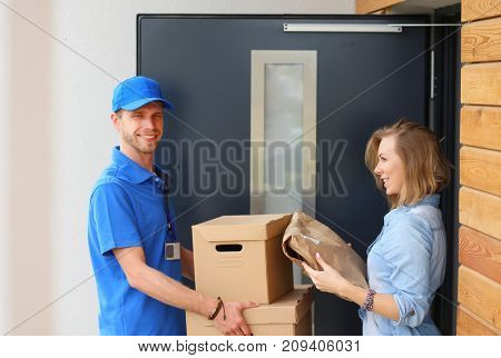 Smiling delivery man in blue uniform delivering parcel box to recipient - courier service concept. Smiling delivery man in blue uniform