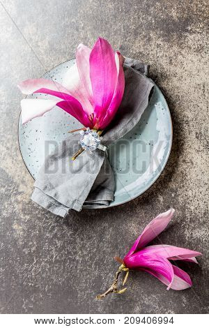 Napkin with srping magnolia flower on gray plate, stone background. Top view.