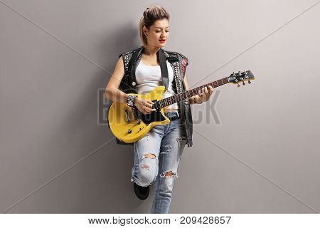 Female punker leaning against a gray wall and playing an electric guitar