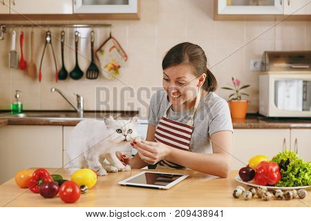 A Young Pretty Woman With White Persian Cat In The Kitchen With Tablet On The Table. Vegetable Salad