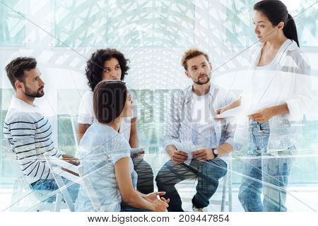 Constructive discussion. Young experienced psychologist standing in front of clients and giving pieces of advice while holding papers with information