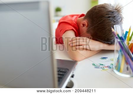 education, cyberbullying and people concept - tired or sad student boy with laptop computer lying on desk at home suffering from bullying