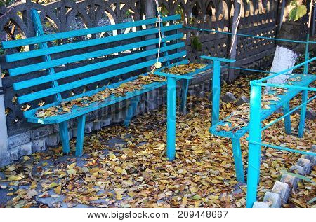 Old blue wooden bench and fallen autumn leaves at a rural dooryard