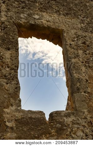 Blue sky with a white cloud seen through a window of a ruined wall