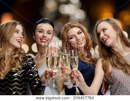holidays, celebration and people concept - happy women clinking non alcoholic champagne glasses at new year party over christmas tree lights background