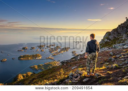 Hiker standing at the top of mount Festvagtinden with views over the village of Henningsvaer. Henningsvaer is a fishing village located on several small islands in the Lofoten archipelago in Norway.