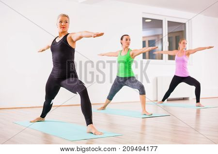 Three girls practicing yoga, Virabhadrasana / Warrior 2 pose