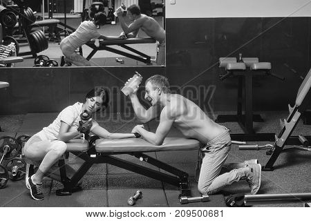 arm wrestling happy couple of pretty woman or cute girl and handsome guy or macho man with muscular torso and sexy body training in sport gym at trainer of weight lifting with water cups