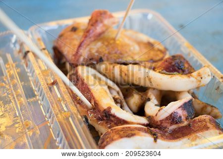 Grilled squid with sauce in transparent plastic tray background