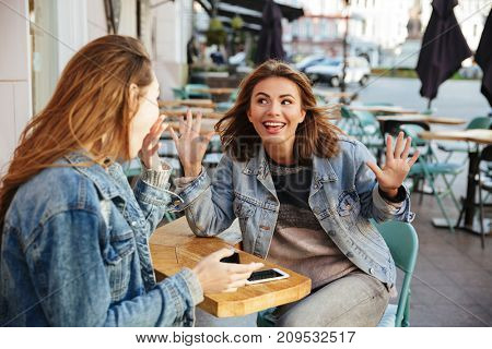 Two pretty brunette woman in keans casual wear having fun while sitting in city cafe