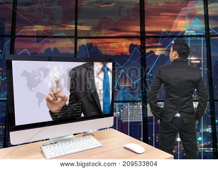 the computer on the wood table with Businessman point sign of money at the screen in front of the glass window over on the trading graph over the blurred photo of cityscapeBack side of Businessman