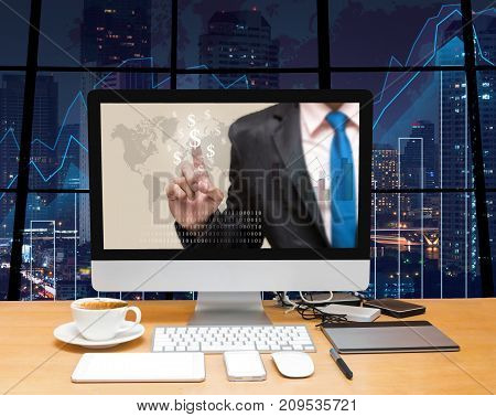 Workspace with computer desktop with Businessman point sign of money at the screen on the trading graph over the blurred photo of cityscape backgroundElements of this image furnished