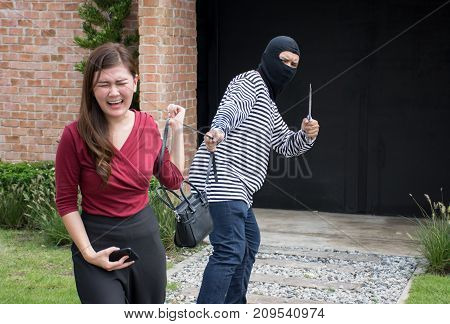 Male robber robbing a handbag threatening with knife to scared Asian woman,criminal concept