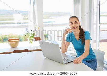 a young woman in casual clothes using the laptop computer in the living room or kitchen. freelance or remote work concept
