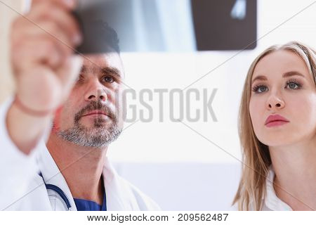 Mature male doctor hold in arm and look at xray photography discussing it with female patient portrait. Bone disease exam medic assistance cancer test healthy lifestyle hospital practice concept