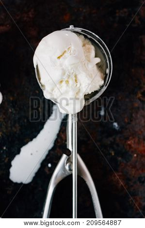 Melted ice cream in metal ice cream scooper over black rustic table