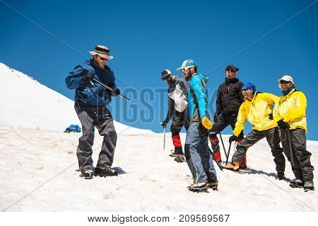 Training to correct slip on a slope or a glacier with the help of an ice ax. A young guide with a beard explains to his group how to properly slow the slip on the slope with the help of an ice ax. Preparation before climbing to the top of the mountain