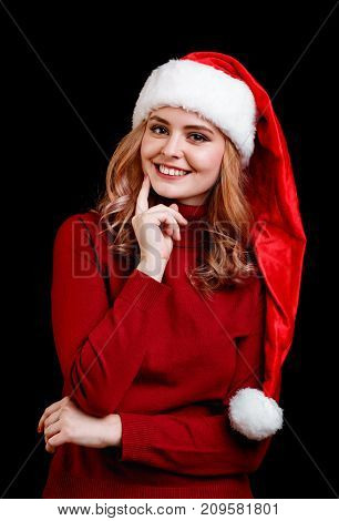 Portrait of a gorgeous girl in a cute festive Santa costume posing on a black background. Cheerful Christmas young woman smiling in a red cap.