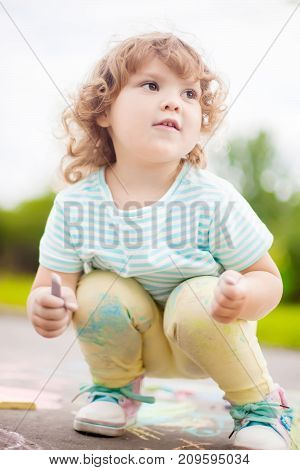 Sunny and warm summer days and happy chilhood. Cute little girl drawing with chalk crayons outdoors.