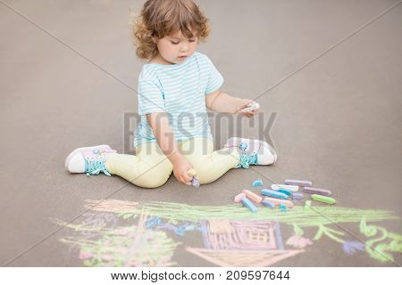 Sunny and warm summer days and happy chilhood. Cute little girl drawing with chalk crayons outdoors.