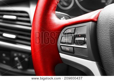 Cruise control buttons on the red steering wheel of a modern car car interior details