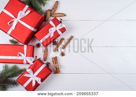 Christmas background with red gift boxes fir tree branches pine cones cinnamon and stars anise free space. Red Christmas gift boxes on white wooden background copy space. Flat lay top view