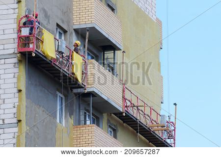 Workers in suspended cradle for facing facade of tall building under construction